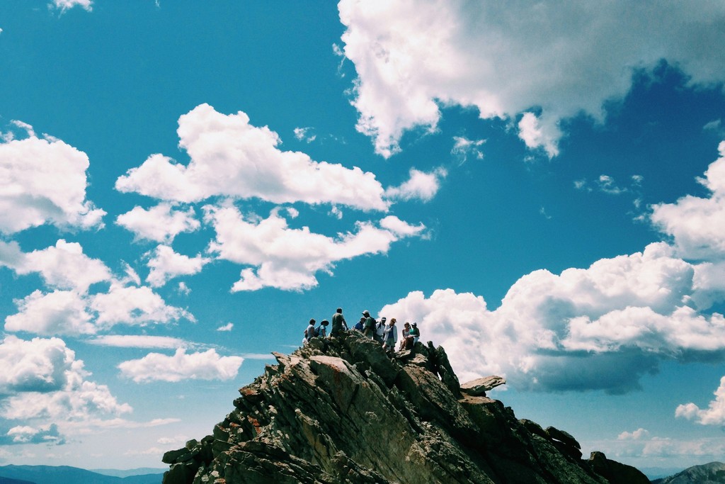 people on rock formation under white cloudy sky